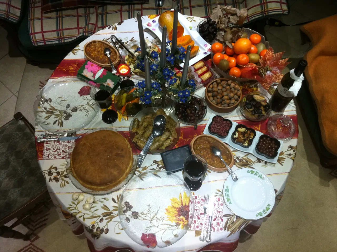 A round table laid for a Macedonian Christmas Eve fast with bean dishes, rolled sarma, a round loaf, pickles, olives, nuts, oranges and red wine