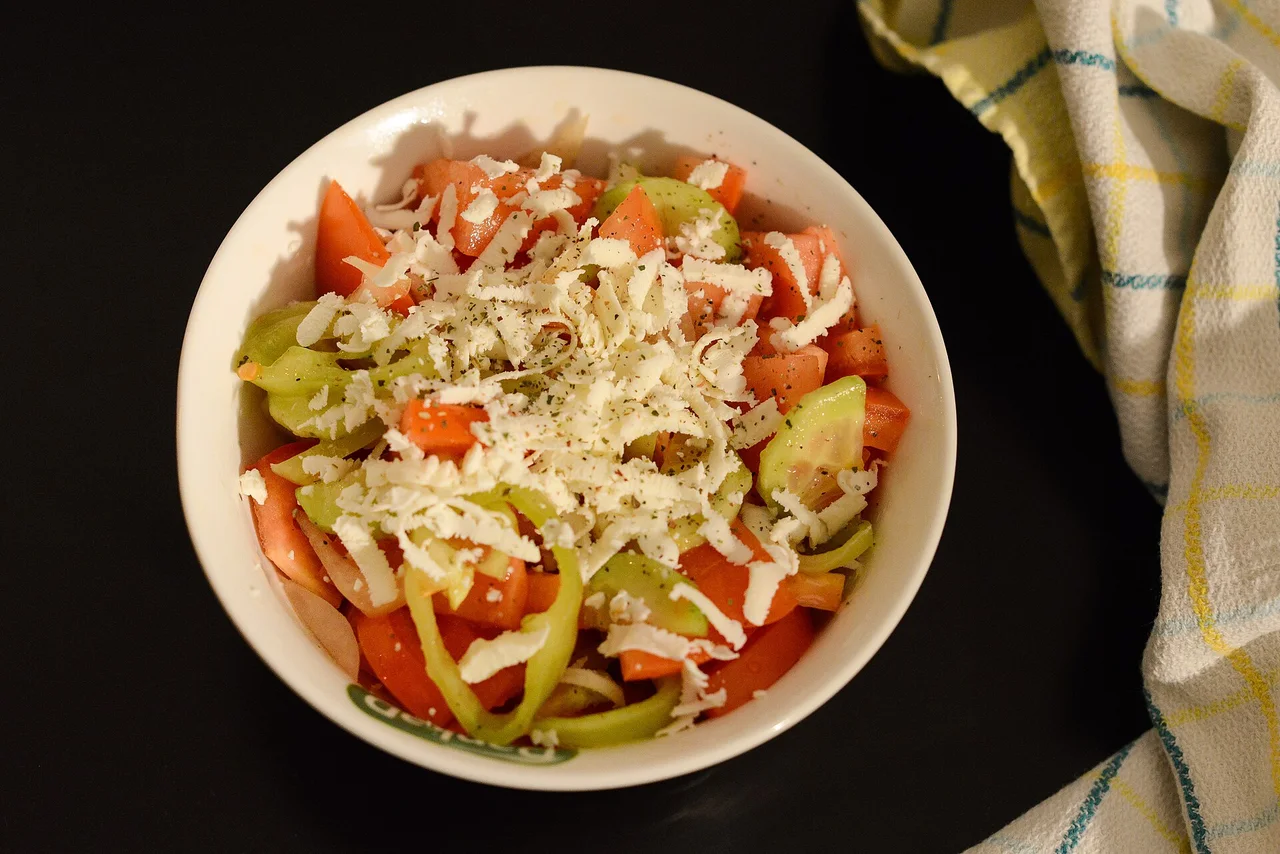A bowl of šopska salad: chopped tomato, cucumber and green pepper under a heap of finely grated white cheese