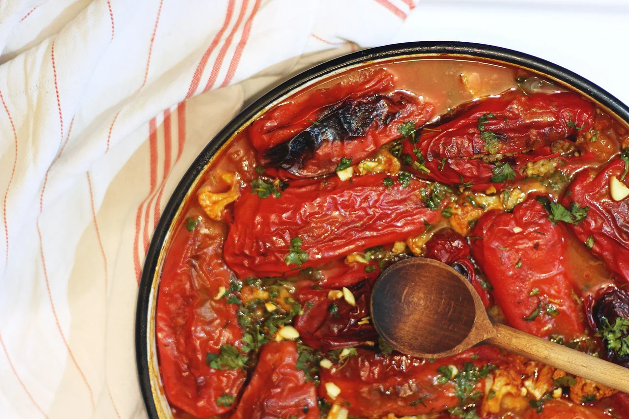 Red peppers stuffed with rice baked in a tomato sauce in a large pan, with a wooden spoon