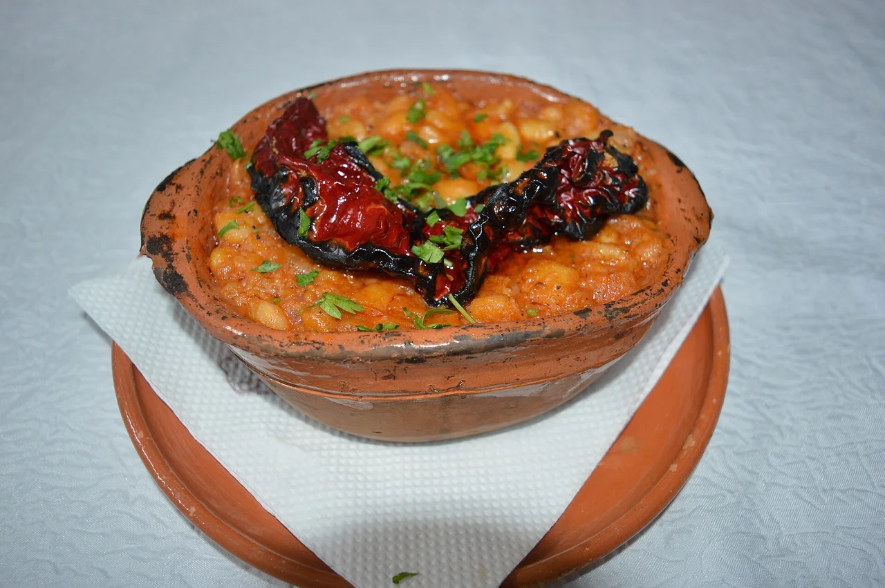 Tavče gravče in a round clay dish, with two roasted dried red peppers and chopped parsley on top