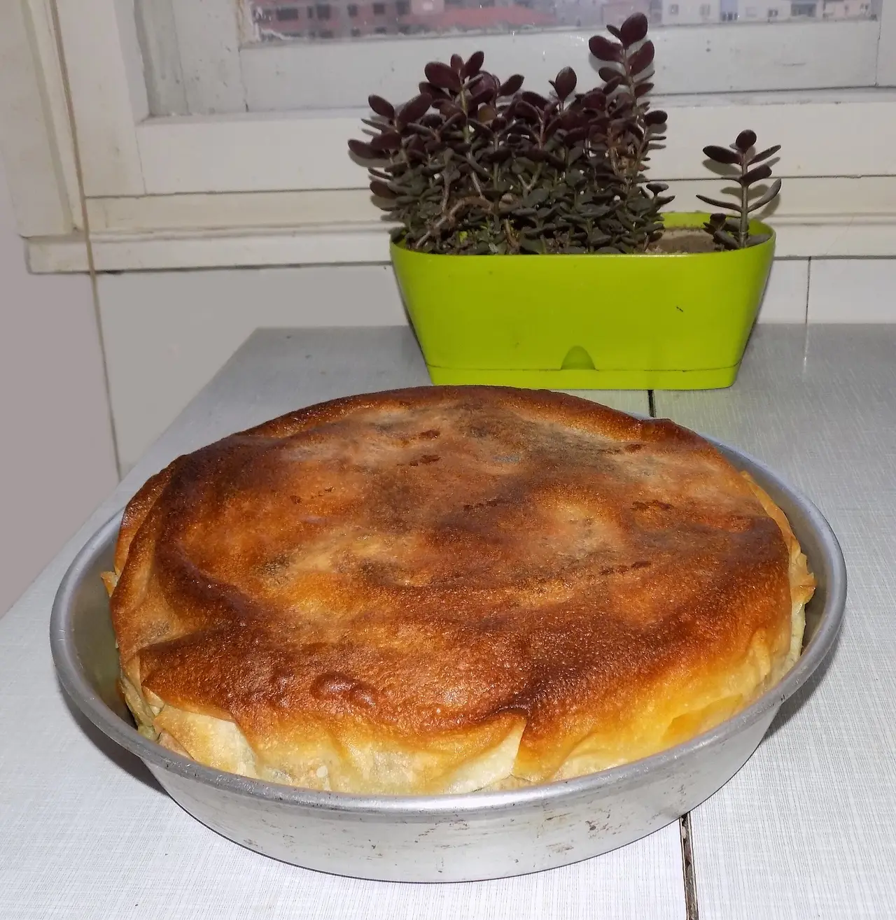 A whole round burek with golden, crisp filo pastry in a metal baking tray
