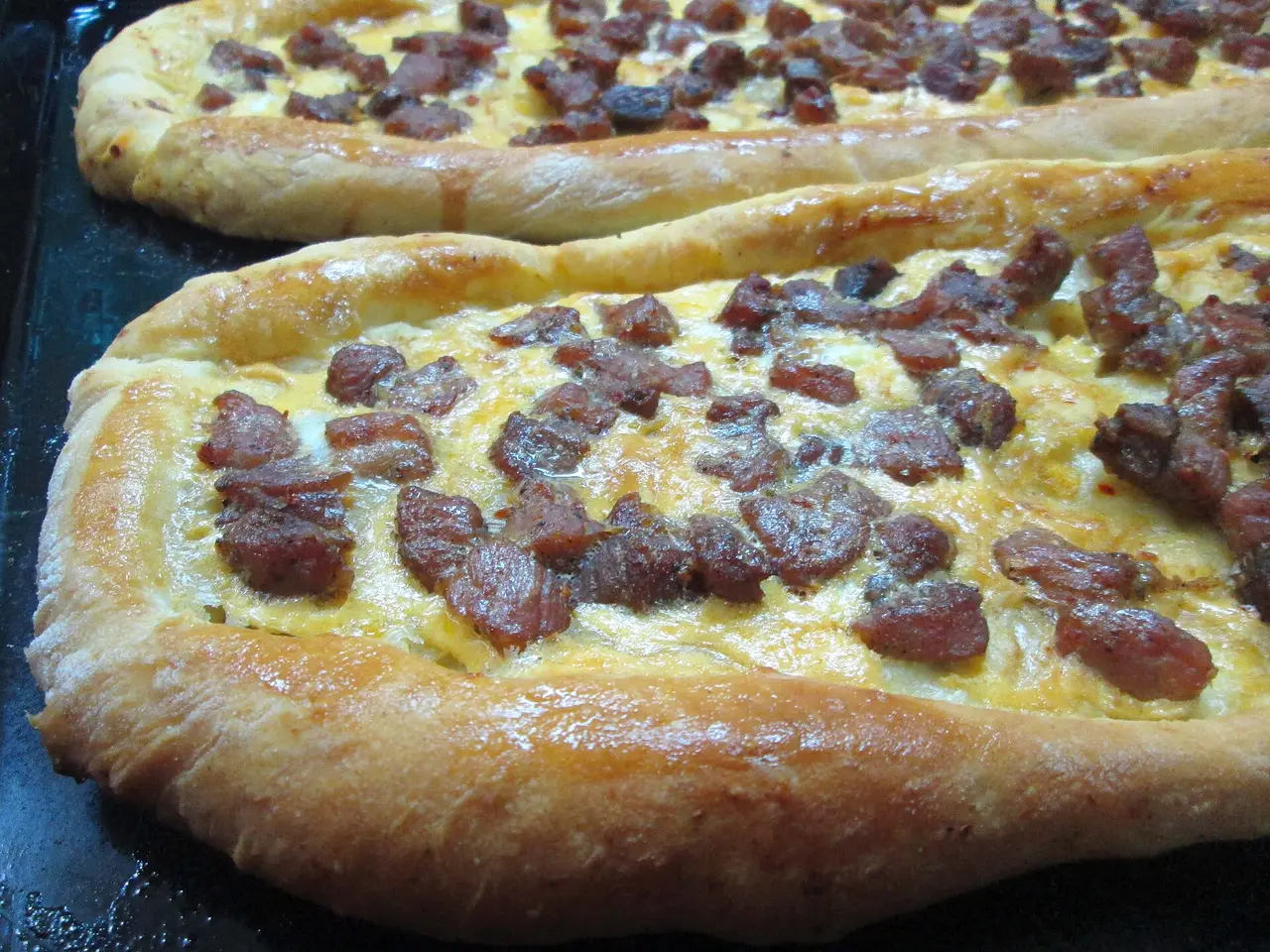 Two oval pastrmajlija flatbreads topped with cubes of browned meat