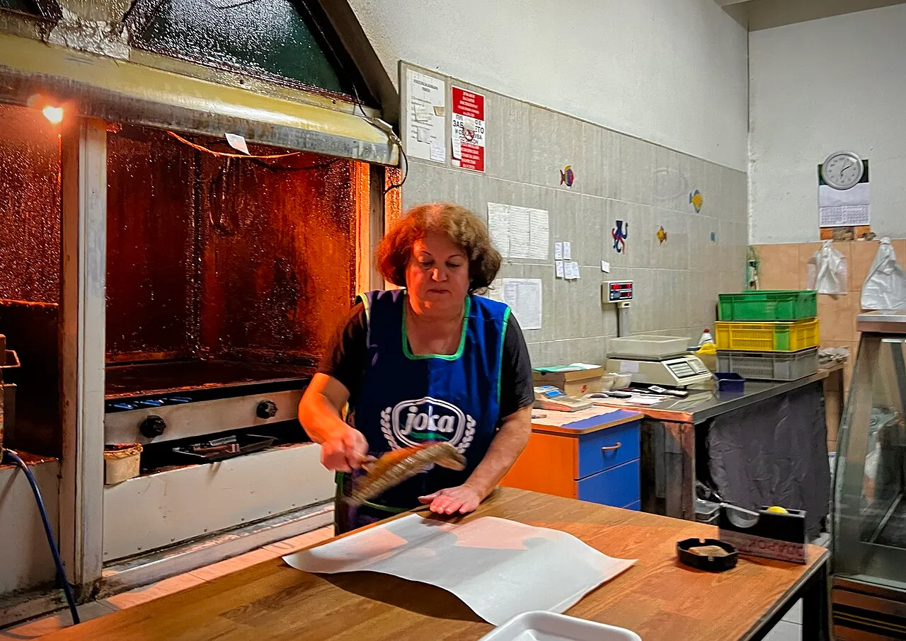 A fishmonger in an apron grilling fish at a small local fish shop in Ohrid