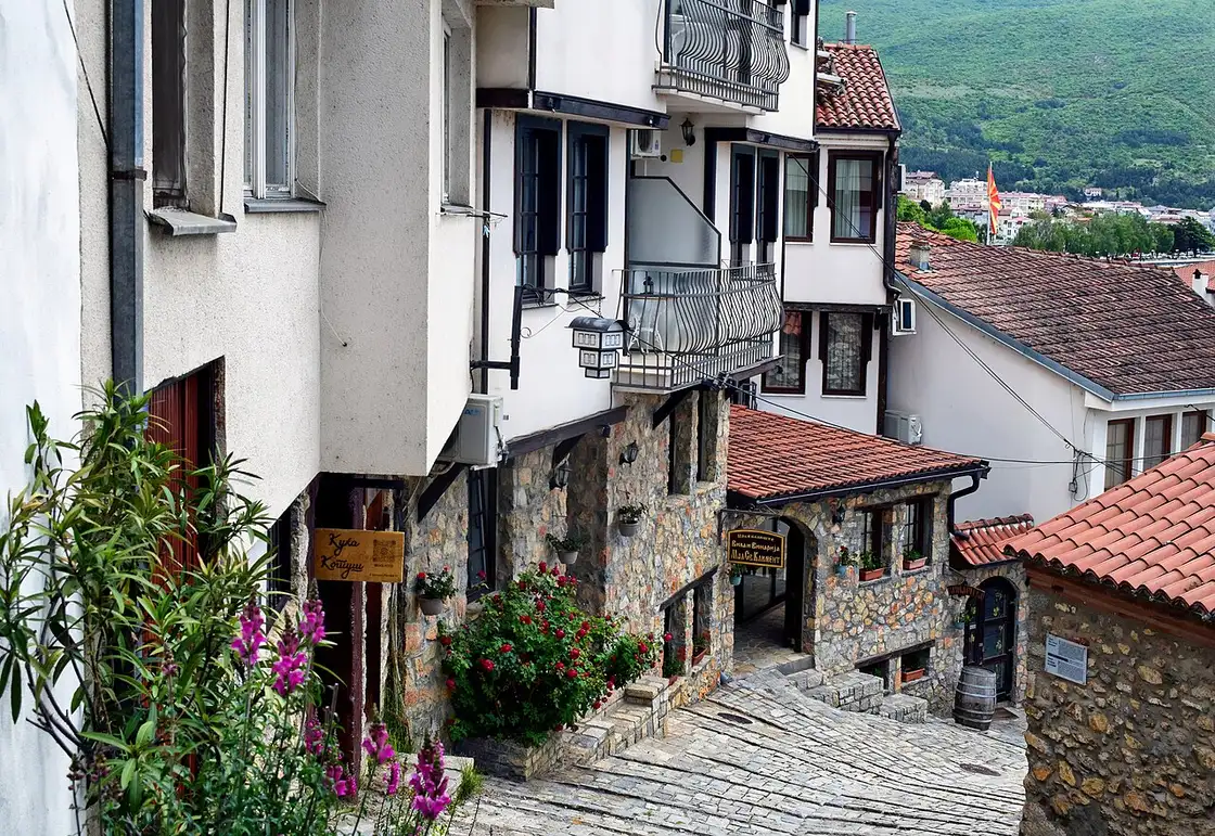 A cobbled stepped lane in Ohrid's old town lined with stone-and-timber houses, a small konak restaurant and flowers