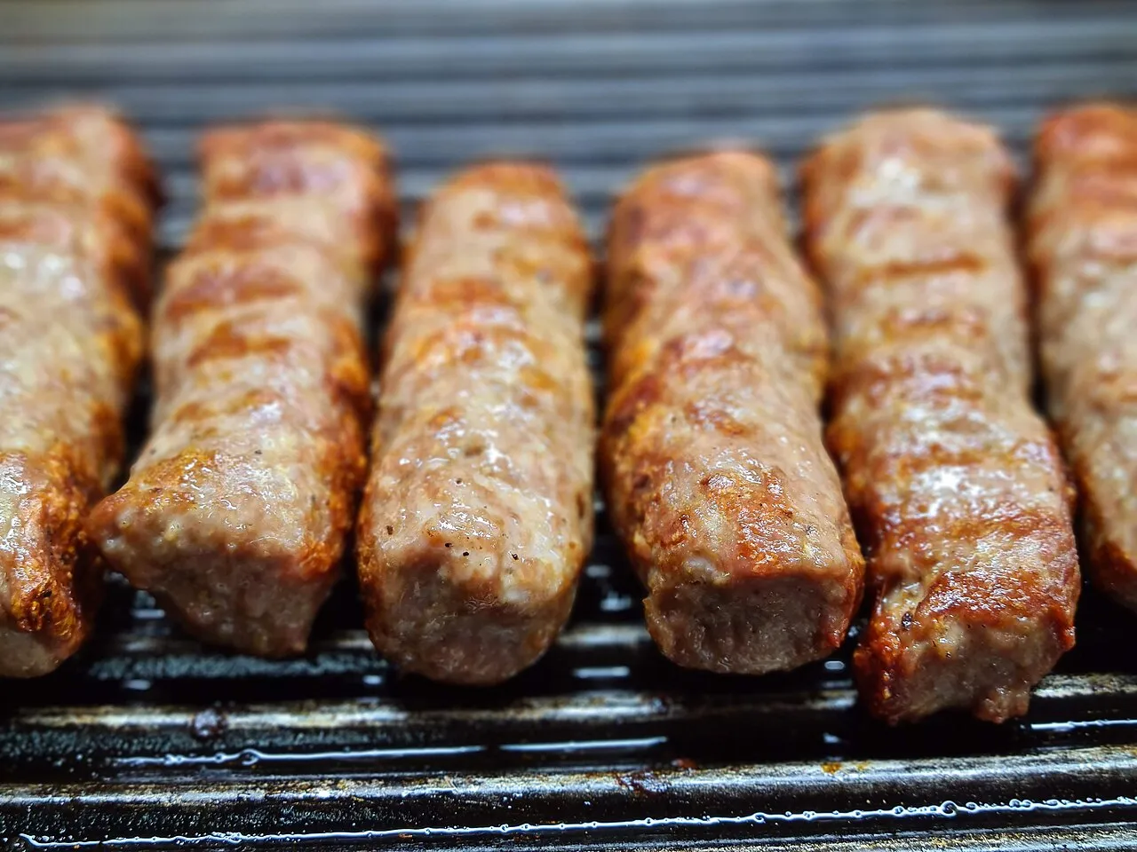 A close row of kebapi grilling over charcoal