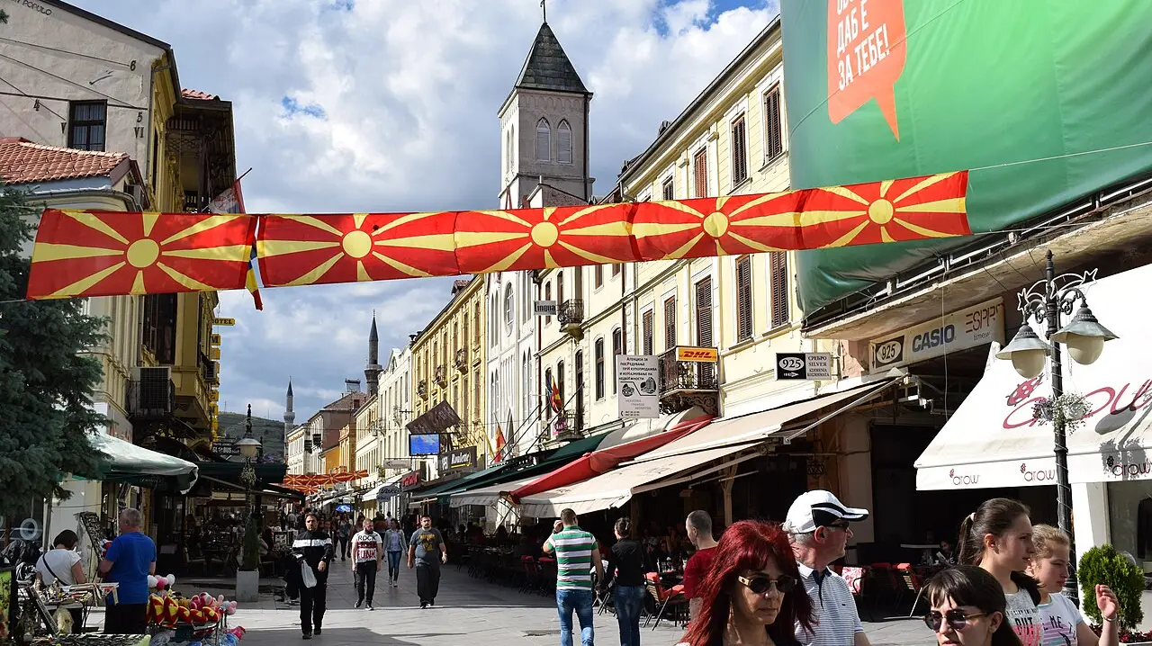 The Široki Sokak pedestrian street in Bitola with café terraces, a Macedonian flag and the clock tower behind, busy with people