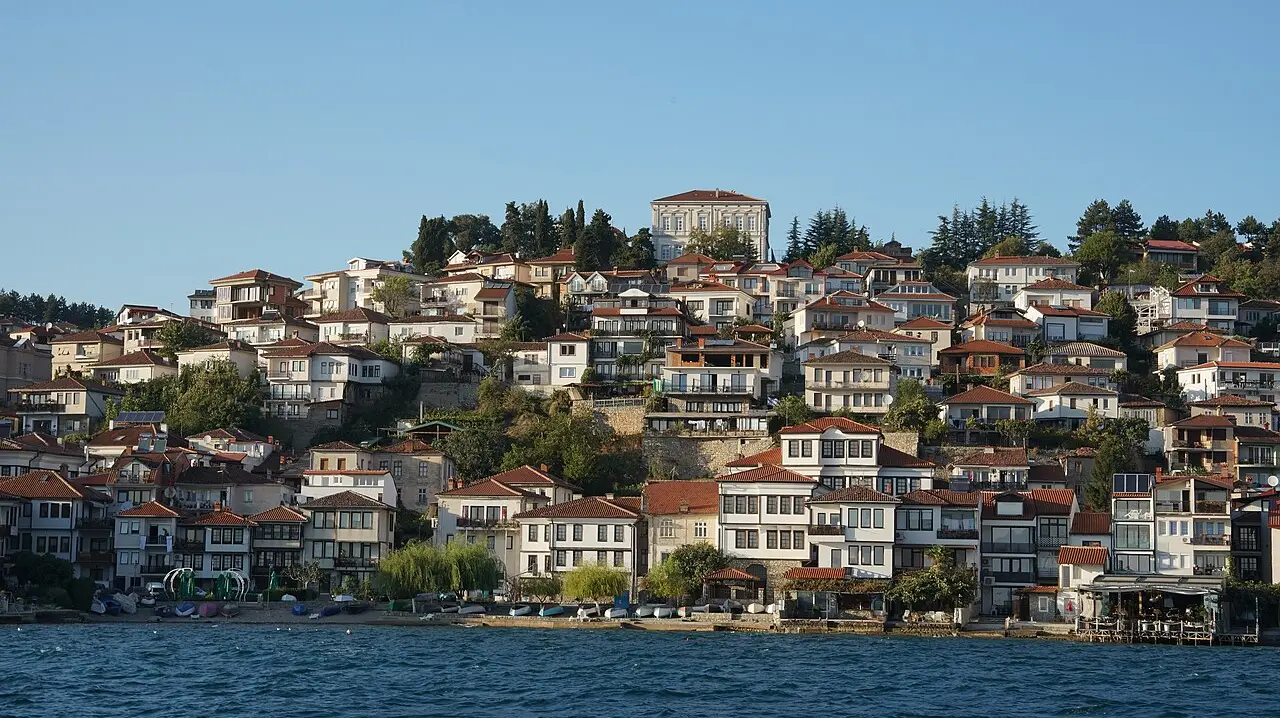 Ohrid old-town houses with red roofs stacked up the hillside above the lakeshore, seen from the water