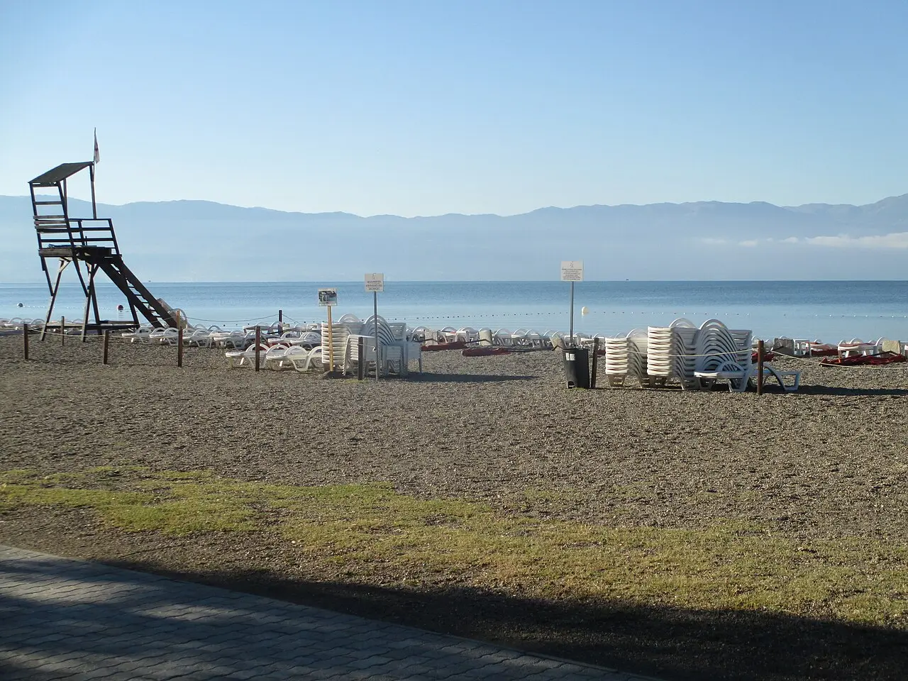 Rows of stacked white sunbeds and a lifeguard tower on a Struga hotel beach in the morning light