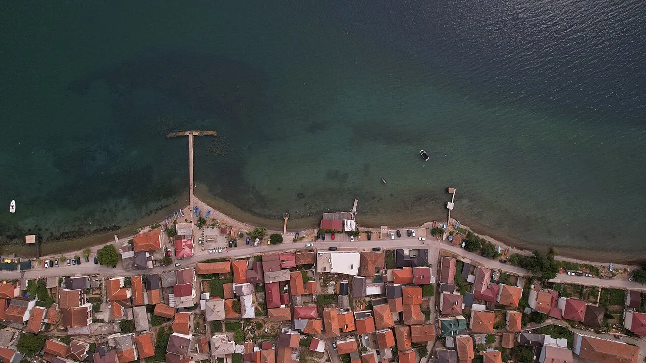 Overhead view of the red roofs of Radozda village along the shore of Lake Ohrid with a jetty and moored boats