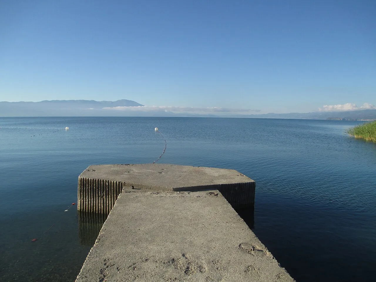 Concrete swimming platform reaching into the flat blue water of Lake Ohrid at Struga with mountains beyond
